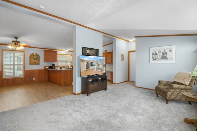 carpeted living room featuring ceiling fan, wooden walls, ornamental molding, a textured ceiling, and vaulted ceiling