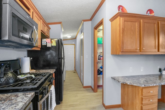 kitchen with crown molding, appliances with stainless steel finishes, built in desk, a textured ceiling, and light wood-type flooring