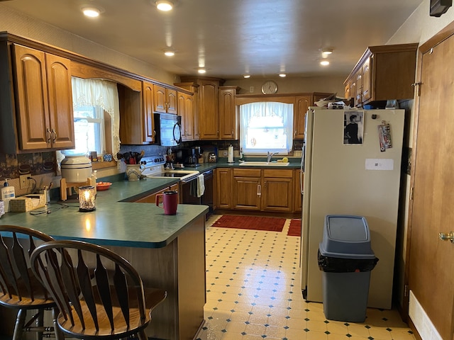 kitchen featuring refrigerator, sink, backsplash, white electric range oven, and kitchen peninsula