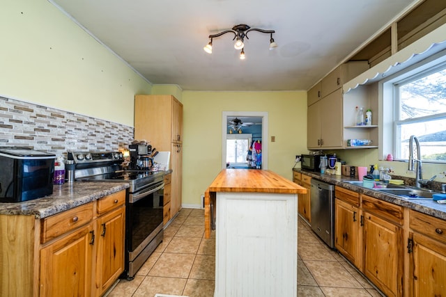 kitchen with sink, light tile patterned floors, appliances with stainless steel finishes, a center island, and wood counters