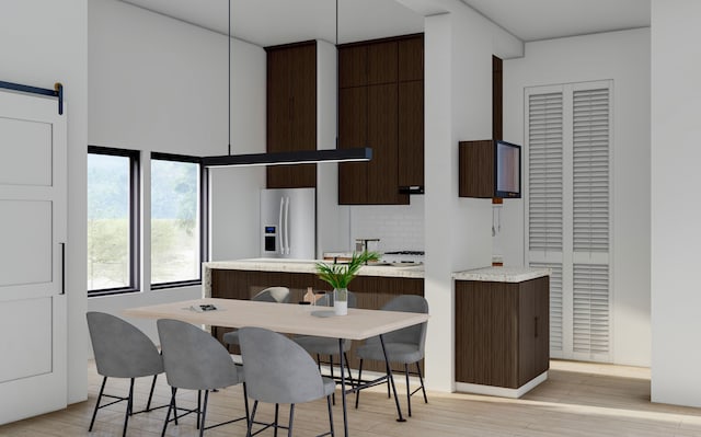 kitchen with stainless steel fridge, a kitchen breakfast bar, tasteful backsplash, light hardwood / wood-style floors, and a barn door