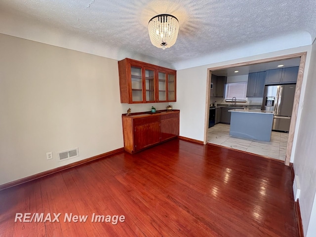 unfurnished living room featuring sink, a notable chandelier, a textured ceiling, and light wood-type flooring