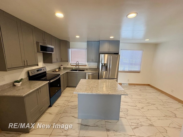 kitchen featuring a kitchen island, sink, gray cabinetry, light stone counters, and stainless steel appliances