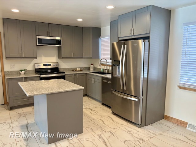 kitchen with gray cabinets, a kitchen island, sink, light stone counters, and stainless steel appliances