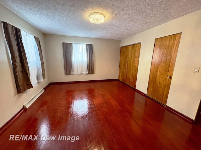 unfurnished bedroom featuring dark hardwood / wood-style flooring, a textured ceiling, multiple closets, and baseboard heating