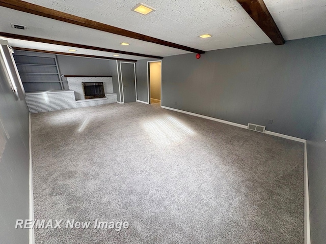 unfurnished living room with a brick fireplace, a textured ceiling, carpet floors, and beamed ceiling