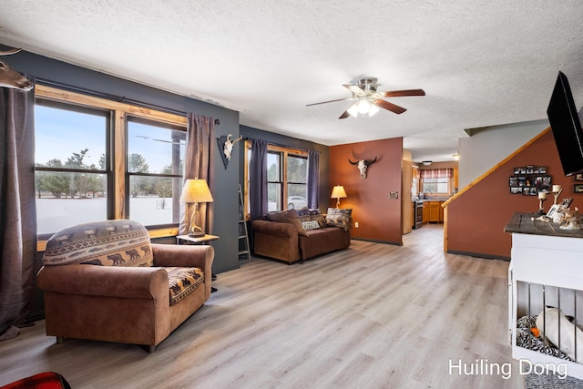 living room featuring ceiling fan, a water view, a textured ceiling, and light wood-type flooring