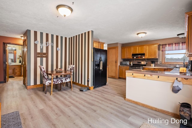 kitchen with stainless steel gas range, black refrigerator with ice dispenser, a textured ceiling, light hardwood / wood-style flooring, and kitchen peninsula