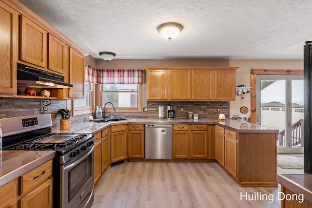 kitchen featuring sink, tasteful backsplash, kitchen peninsula, stainless steel appliances, and light hardwood / wood-style floors