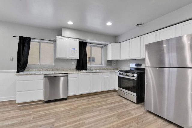 kitchen featuring appliances with stainless steel finishes, sink, white cabinets, light hardwood / wood-style floors, and light stone countertops