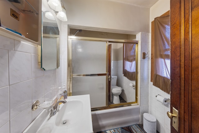 full bathroom featuring tile walls, sink, toilet, and combined bath / shower with glass door