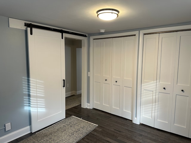 unfurnished bedroom featuring dark hardwood / wood-style floors, multiple closets, and a barn door