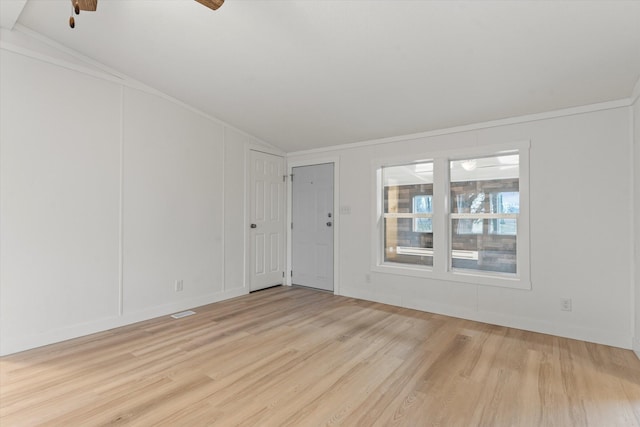 empty room with ornamental molding, vaulted ceiling, and light hardwood / wood-style floors