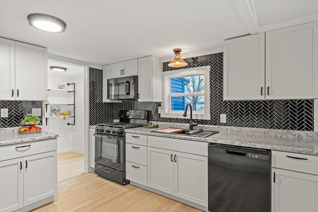 kitchen with white cabinetry, sink, light stone counters, black appliances, and light wood-type flooring