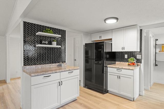 kitchen featuring backsplash, light stone countertops, light hardwood / wood-style floors, white cabinets, and black fridge