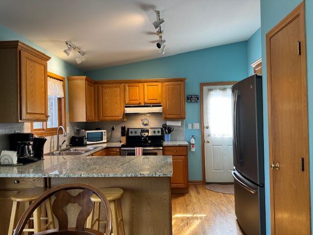 kitchen with black refrigerator, sink, a kitchen bar, and stainless steel range with electric stovetop