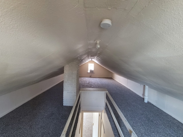 additional living space with dark carpet, vaulted ceiling, and a textured ceiling