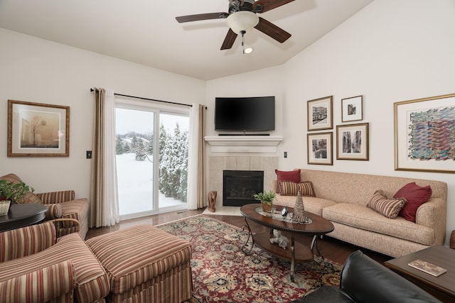 living room with ceiling fan, lofted ceiling, a tiled fireplace, and wood-type flooring