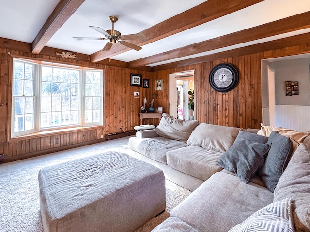 carpeted living room with wooden walls, ceiling fan, and beam ceiling