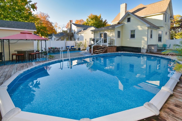 view of swimming pool featuring a wooden deck, exterior bar, and a gazebo