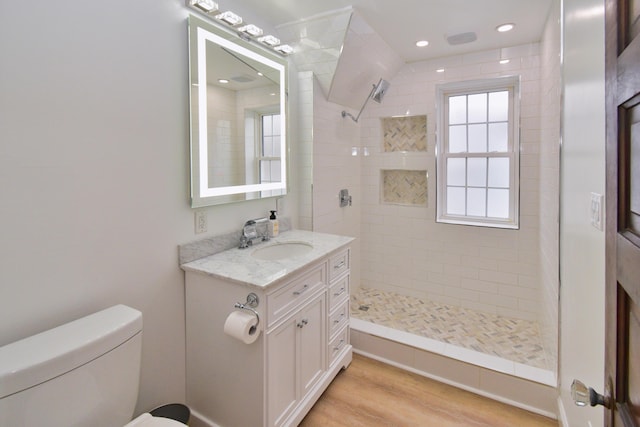 bathroom with hardwood / wood-style flooring, vanity, toilet, and a tile shower