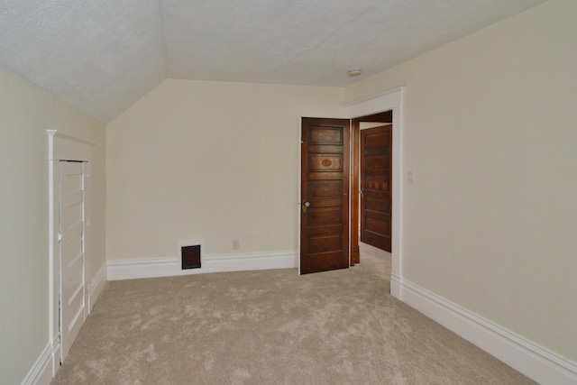 unfurnished room featuring lofted ceiling, light carpet, and a textured ceiling