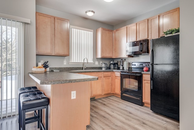 kitchen with sink, black appliances, a breakfast bar, and light brown cabinets