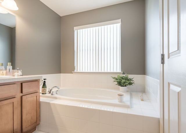 bathroom with a relaxing tiled tub, a healthy amount of sunlight, and vanity