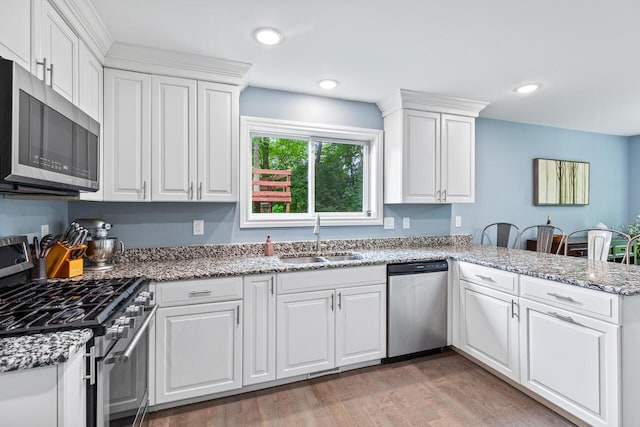 kitchen with sink, white cabinetry, kitchen peninsula, stainless steel appliances, and hardwood / wood-style floors