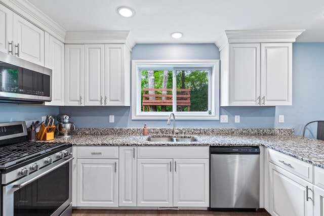 kitchen with appliances with stainless steel finishes, sink, white cabinets, and light stone counters