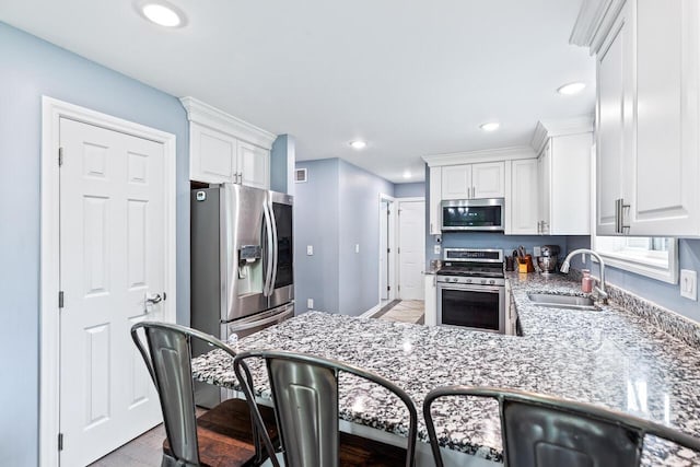 kitchen featuring sink, appliances with stainless steel finishes, white cabinetry, light stone counters, and kitchen peninsula