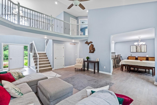 living room with a towering ceiling, light hardwood / wood-style flooring, and ceiling fan with notable chandelier