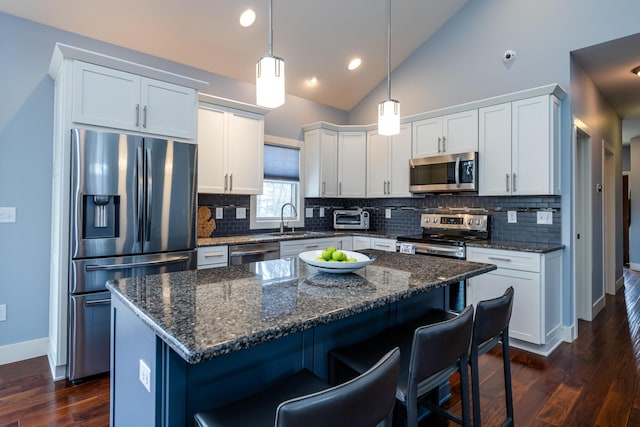 kitchen with sink, stainless steel appliances, white cabinets, a kitchen island, and decorative light fixtures