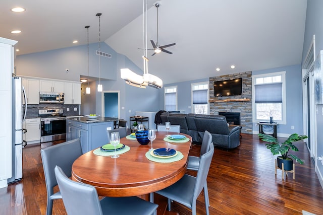 dining area featuring ceiling fan with notable chandelier, a fireplace, dark hardwood / wood-style flooring, and high vaulted ceiling