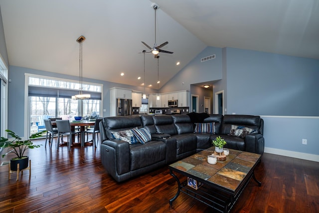 living room featuring ceiling fan with notable chandelier, dark wood-type flooring, and high vaulted ceiling