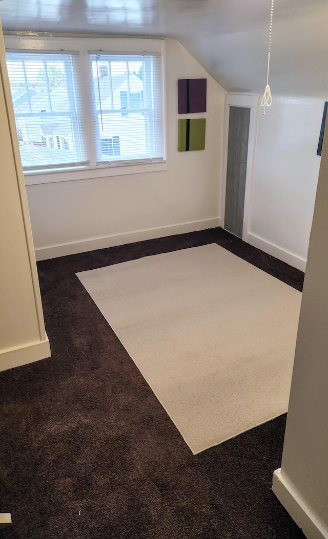 additional living space featuring lofted ceiling and dark colored carpet