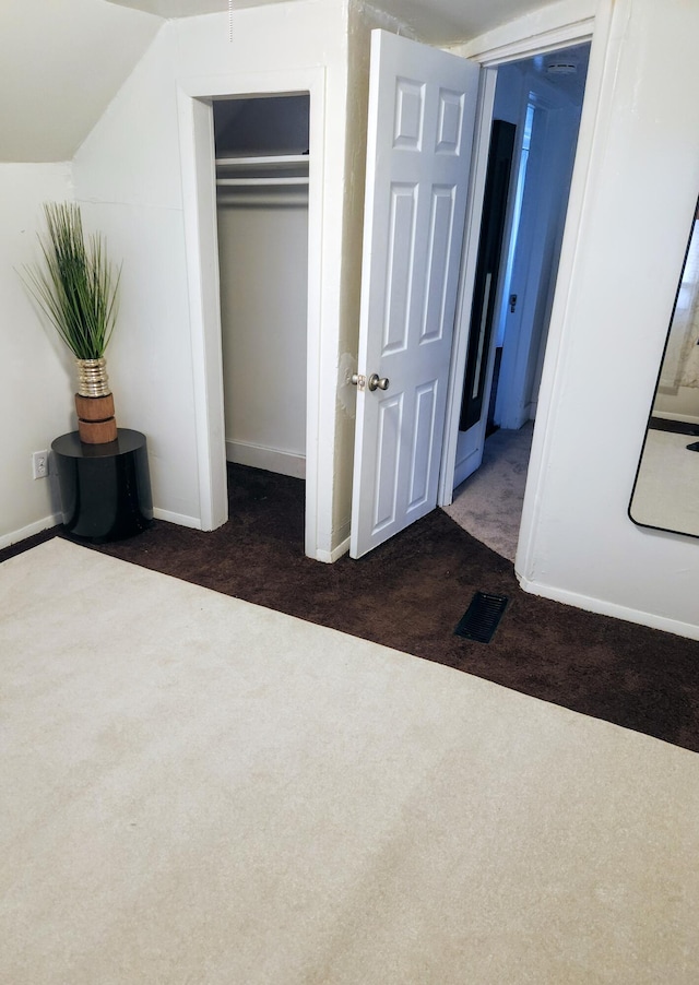 unfurnished bedroom featuring lofted ceiling, a closet, and dark colored carpet