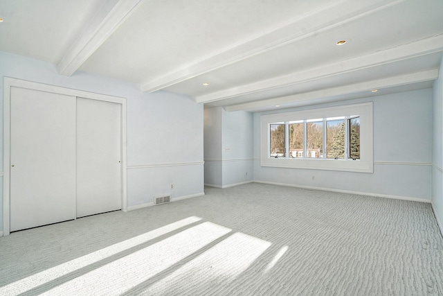 unfurnished bedroom with light colored carpet, beam ceiling, and a closet