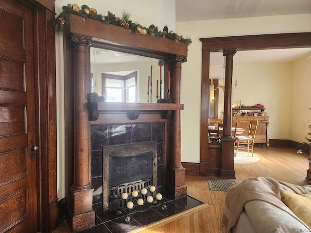 living room featuring a tiled fireplace, wood-type flooring, and ornate columns