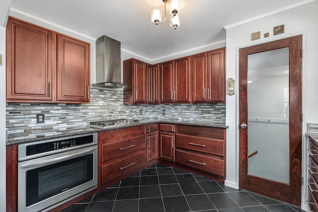 kitchen featuring appliances with stainless steel finishes, decorative backsplash, dark tile patterned floors, dark stone counters, and wall chimney range hood