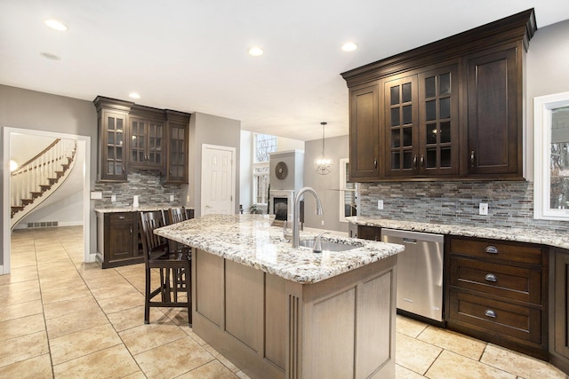 kitchen with sink, a breakfast bar, dishwasher, dark brown cabinetry, and an island with sink