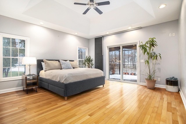 bedroom featuring multiple windows, access to exterior, a tray ceiling, and light hardwood / wood-style floors