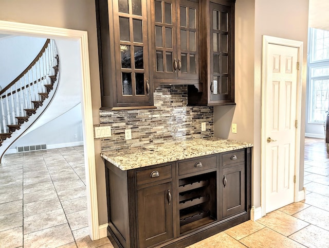 bar with light stone counters, light tile patterned floors, dark brown cabinets, and tasteful backsplash