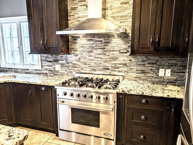 kitchen featuring dark brown cabinetry, light stone counters, stainless steel range, wall chimney range hood, and backsplash