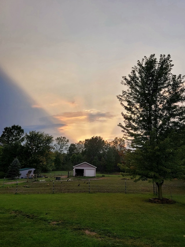 yard at dusk with a garage, an outbuilding, and a rural view