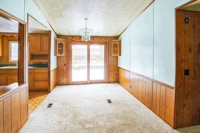 dining space with light carpet, a wealth of natural light, a chandelier, and wood walls