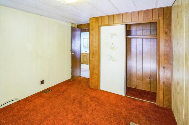 unfurnished bedroom with carpet flooring, a closet, and wood walls