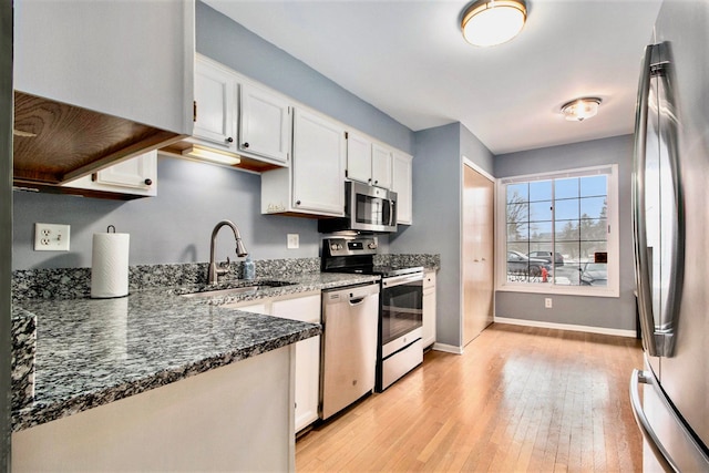 kitchen with appliances with stainless steel finishes, sink, dark stone countertops, and white cabinets