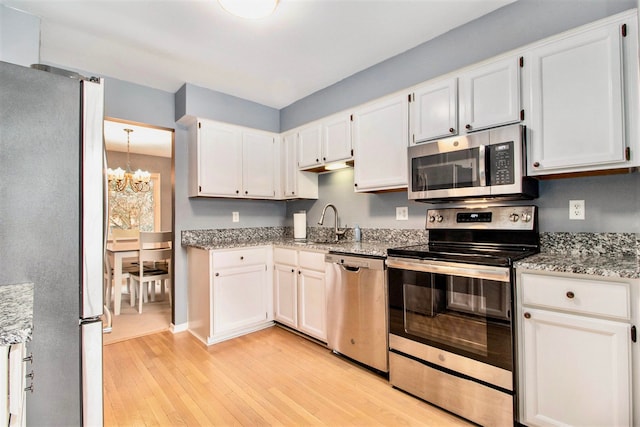 kitchen with a chandelier, light wood-type flooring, stainless steel appliances, light stone countertops, and white cabinets