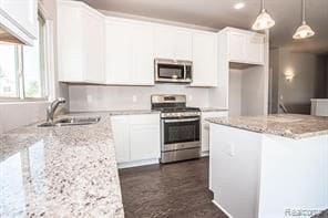 kitchen featuring hanging light fixtures, appliances with stainless steel finishes, white cabinetry, a sink, and a kitchen island